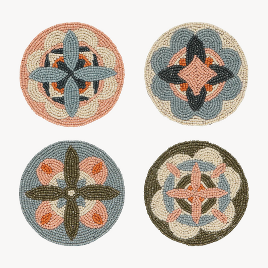 Four round woven coasters with geometric and floral mandala patterns in muted tones of blue, orange, beige, and olive green, arranged in a 2x2 grid on a light off-white background.